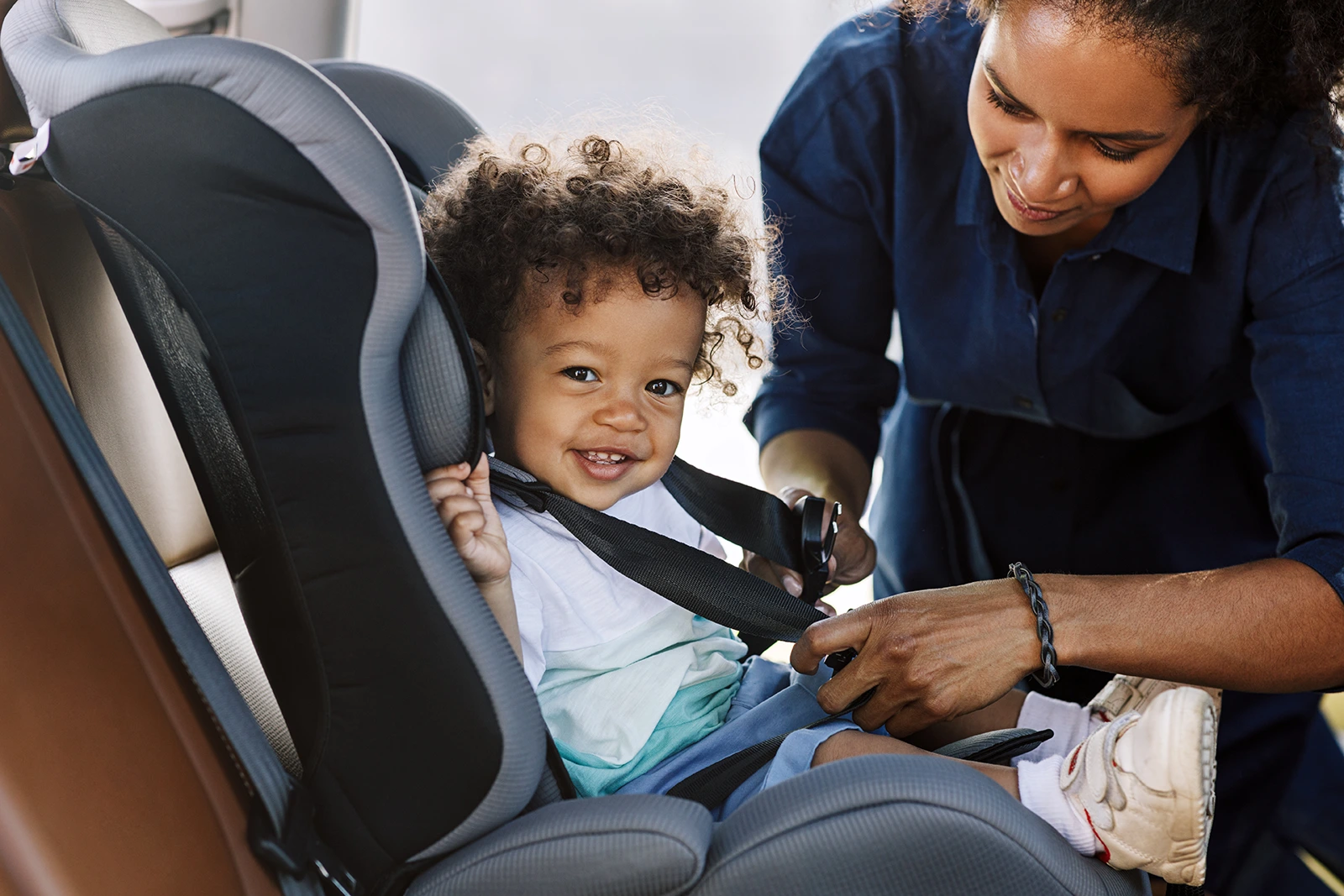 Mom buckling happy child into car seat.