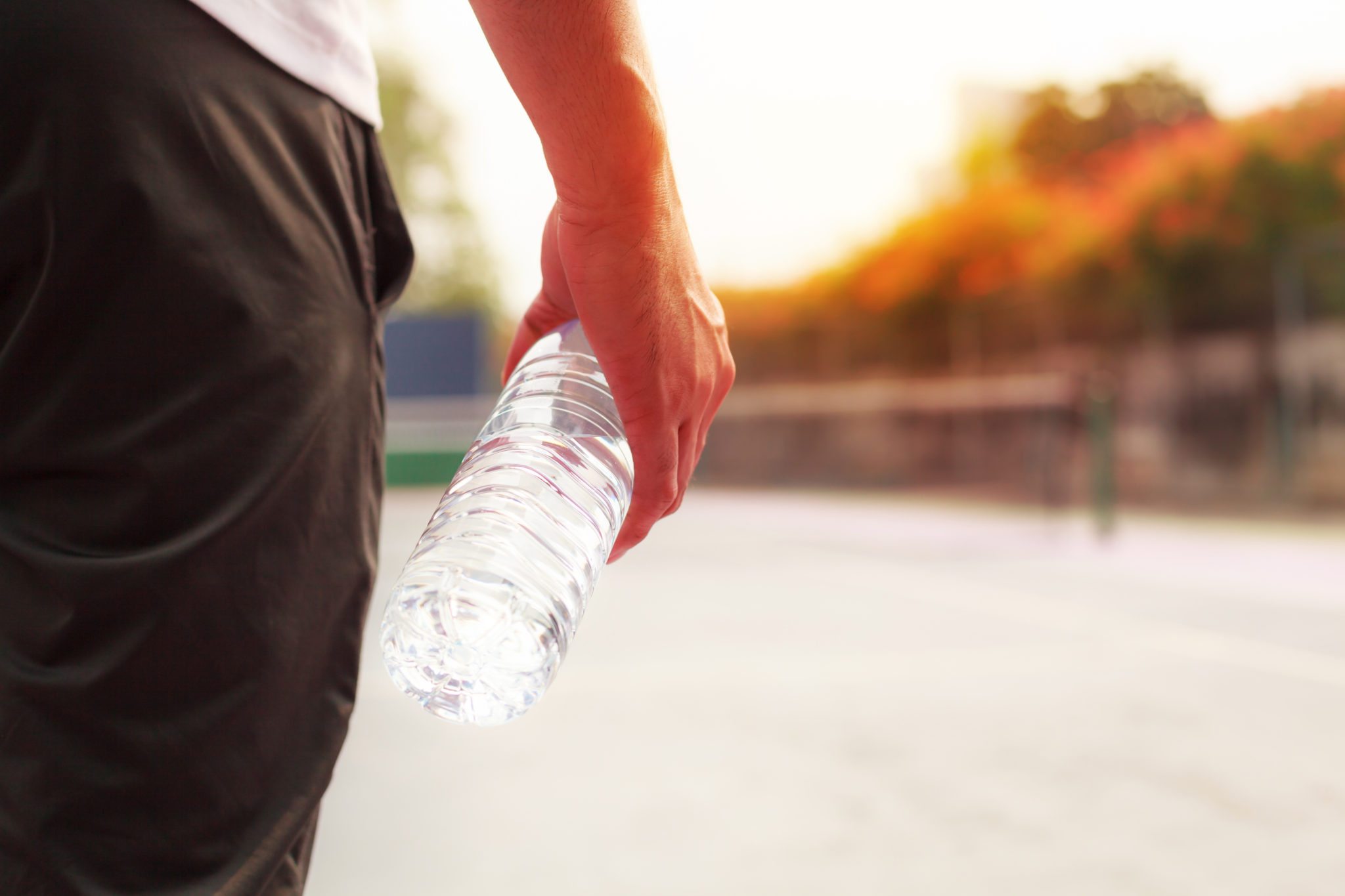 Exhausted man holding clear drinking water bottle after playing sport on sunset background
