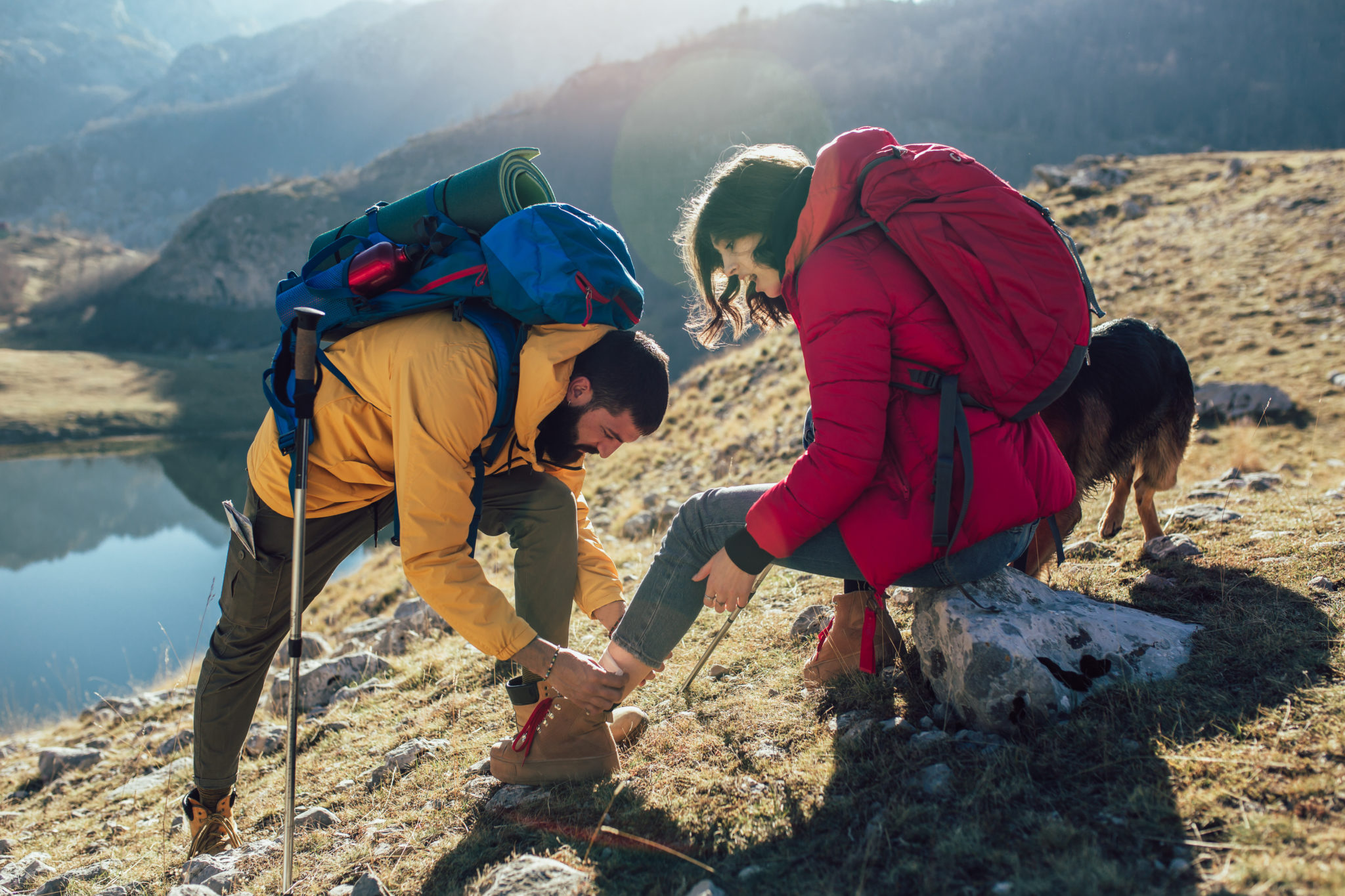 A woman has sprained her ankle while hiking, her friend uses the first aid kit to tend to the injury